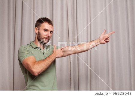 Portrait of confident adult man in green t-shirt pointing up against beige background 96928043