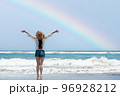 虹の出たビーチで両手を広げる女性 96928212