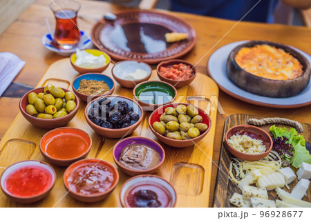 Turkish breakfast table. Pastries, vegetables, greens, olives, cheeses, fried eggs, spices, jams, honey, tea in copper pot and tulip glasses, wide composition 96928677