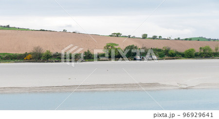 Seaside landscape and a farmer's field on a hill. Sandy seashore on a cloudy day. Calm water surface. The remains of an old ship on the shore. A plowed field. Minimalistic landscape. 96929641