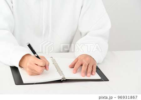 机でシステム手帳にペンで記入する若い男性の手元 96931867