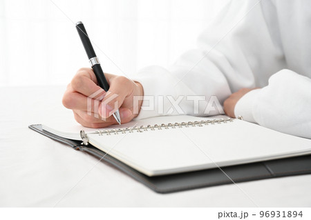 机でシステム手帳にペンで記入する若い男性の手元 96931894