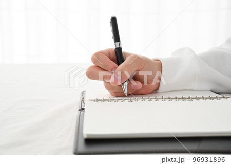 机でシステム手帳にペンで記入する若い男性の手元 96931896