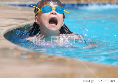 Young child girl in goggles learning to swim in blue pool water outdoors. Summer recreation activity concept 96943384