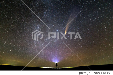 Small silhouette of a scientist with flashlight on his head pointing bright beam of light on starry sky with C/2020 F3 (NEOWISE) comet with light tail. Space exploration concept. Small silhouette of a scientist with flashlight on his head pointing bright beam of light on starry sky with C/2020 F3 (NEOWISE) comet with light tail. Space exploration concept. 96944835