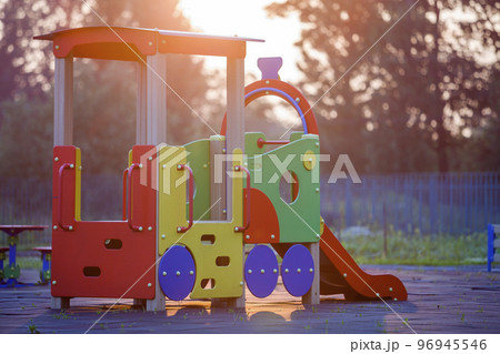 Nursery playground with colorful slides on soft rubber flooring with no children at sunset or sunrise. 96945546