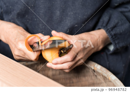 包丁で渋柿の皮を剥いているシニア女性 96948782