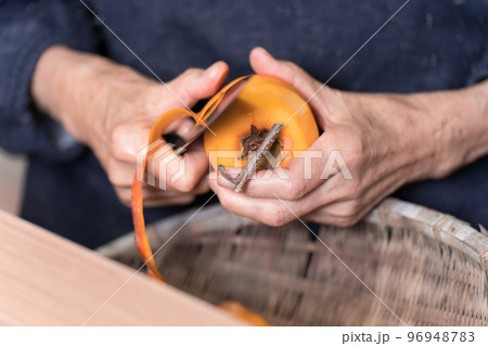 包丁で渋柿の皮を剥いているシニア女性 96948783