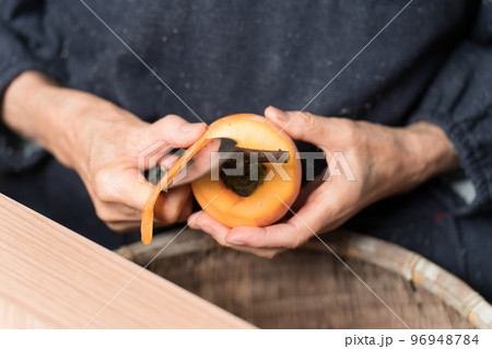 包丁で渋柿の皮を剥いているシニア女性 96948784