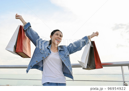 Carefree and overjoyed Asian female carrying her shopping bags, happy with Black Friday sales. Carefree and overjoyed Asian female carrying her shopping bags, happy with Black Friday sales. 96954922