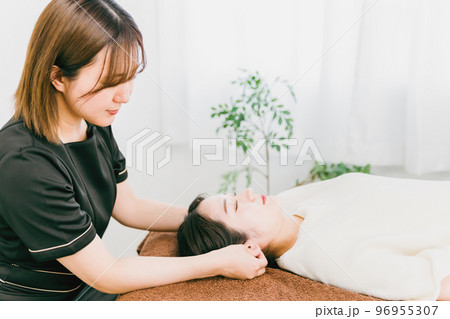 整骨院・鍼灸院で耳ツボマッサージの施術を受けるアジア人女性とセラピスト 96955307
