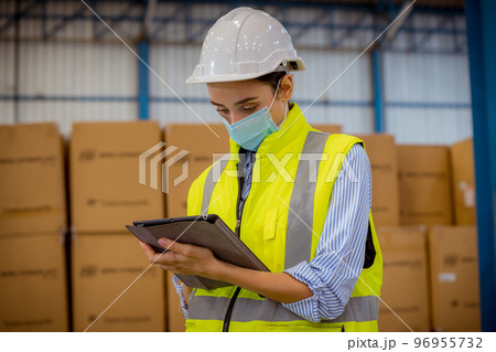 Factory engineer under inspection and checking quality production process on face mask manufacture station by wearing casual uniform and safety helmet in factory plantation. 96955732