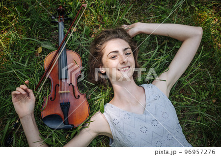 The girl lies with a violin on the grass in a city park. The girl lies with a violin on the grass in a city park. 96957276