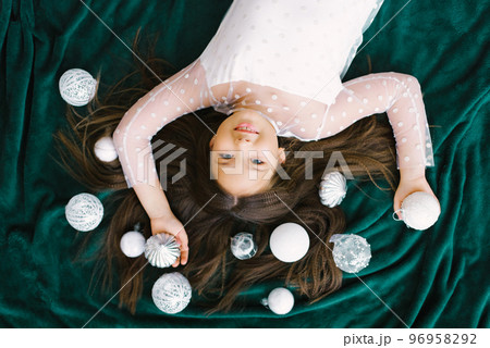 Cute girl with long hair with Christmas decor, white Christmas toys lying on an emerald blanket 96958292