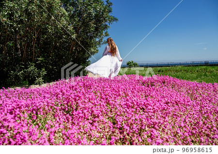a beautiful woman in a white flowing long dress stay near a beautiful field with pink flowers rear view a beautiful woman in a white flowing long dress stay near a beautiful field with pink flowers rear view 96958615