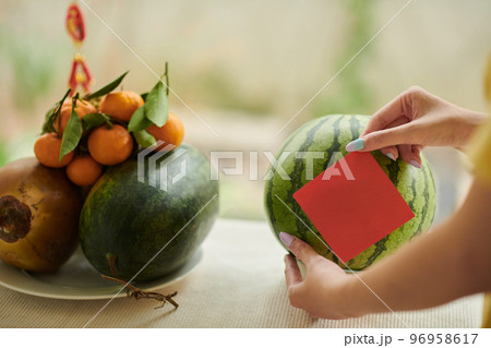 Hands sticking red note on ripe watermelon prepared for Tet celebration Hands sticking red note on ripe watermelon prepared for Tet celebration 96958617
