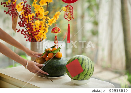 Hands of woman putting fresh fruits on table decorated for Tet celebration Hands of woman putting fresh fruits on table decorated for Tet celebration 96958619