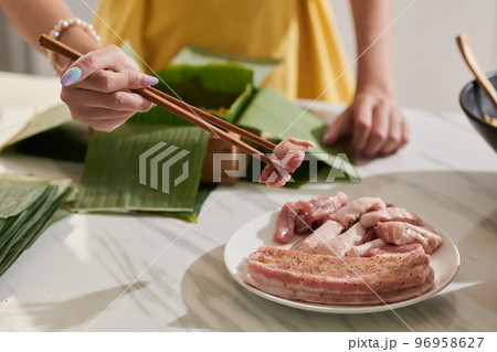 Woman adding pork pieces in mold covered with banana leaves 96958627