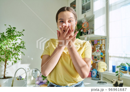 Surprised teenage girl covering mouth with hands looking at camera in home 96961687