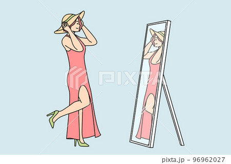 Woman in dress, shoes, tries on hat in front of mirror. 96962027