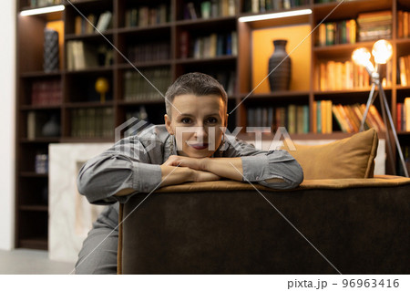 confident woman sitting in an armchair against the backdrop of a cozy home library confident woman sitting in an armchair against the backdrop of a cozy home library 96963416