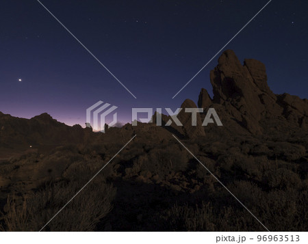 Long exposure night shot of Roques de Garcia volcanic rock formation at El Teide national park, early night winter sky with stars on pink blue glow. Tenerife Canary islands, Spain Long exposure night shot of Roques de Garcia volcanic rock formation at El Teide national park, early night winter sky with stars on pink blue glow. Tenerife Canary islands, Spain 96963513