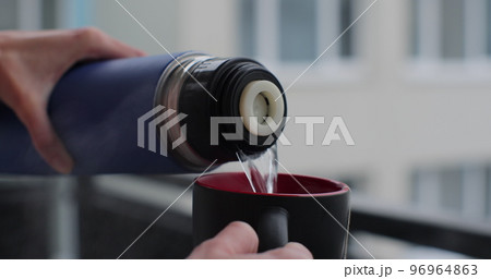 A woman pours herbal tea from a thermos, close-up. 96964863