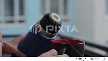 A woman pours herbal tea from a thermos, close-up. 96964864