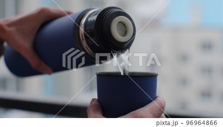 Close-up of woman hand pouring warm tea into the steel cup from thermos. 96964866