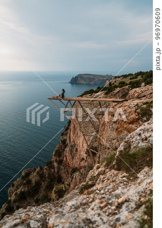 A girl sits on a wooden springboard for jumping with a rope. In a dark green dress with her hands in the air. A girl sits on a wooden springboard for jumping with a rope. In a dark green dress with her hands in the air. 96970609