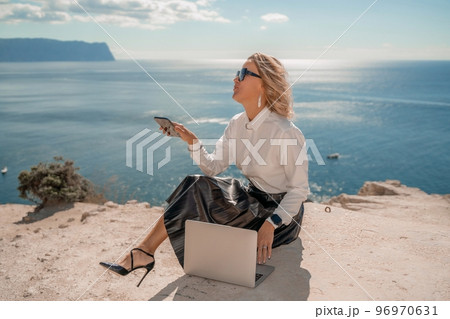 Freelance women sea. She is working on the computer. Good looking middle aged woman typing on a laptop keyboard outdoors with a beautiful sea view. The concept of remote work. 96970631