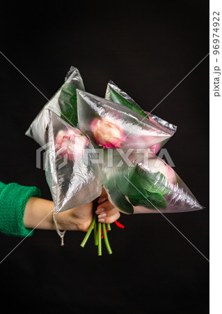 Hand holding bouquet of flowers covered with plastic bags. Isolated on black background. Hand holding bouquet of flowers covered with plastic bags. Isolated on black background. 96974922