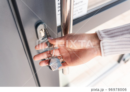 A woman's hand opens the door with a key on which the keychain hangs at home. A woman's hand opens the door with a key on which the keychain hangs at home. 96978006