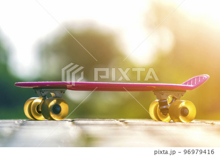 Close-up of child plastic pink skateboard isolated on pavement against bright white and green blurred bokeh background. Sport, recreation, fun and plays concept. Close-up of child plastic pink skateboard isolated on pavement against bright white and green blurred bokeh background. Sport, recreation, fun and plays concept. 96979416