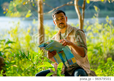 Asian man hold map and sit in the forest with relax during travel and camping in national park. 96979501
