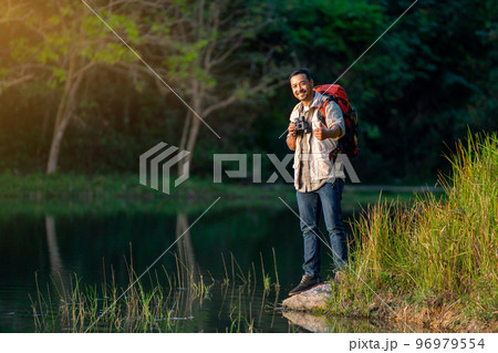 Smart man with backpack accessories look at camera and show thumbs up also stand near lake 96979554