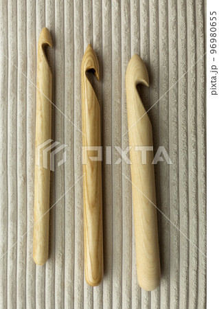 Assorted wooden knitting needles lie on a wooden table, in the background a blurred gray plaid merino wool 96980655