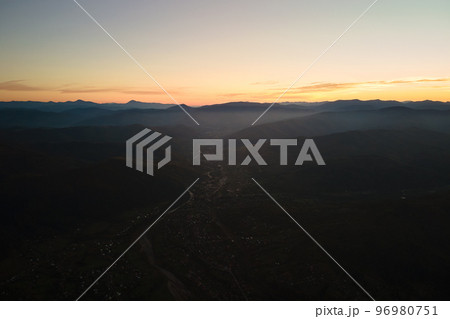 Aerial view of dark mountain hills at sunset. Hazy peaks and misty valleys in evening Aerial view of dark mountain hills at sunset. Hazy peaks and misty valleys in evening 96980751