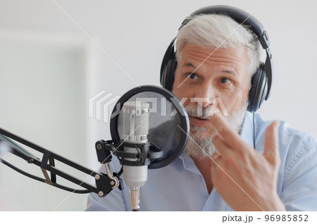 older man with gray hair irecording podcast in recording studio with microphone and headphones 96985852