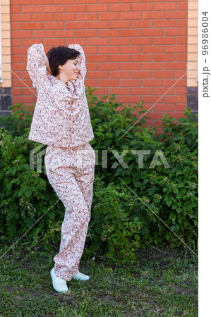 Cheerful woman in home wear pajama outdoor brick wall backyard background emotions - sleepwear and homewear concept Cheerful woman in home wear pajama outdoor brick wall backyard background emotions - sleepwear and homewear concept 96986004