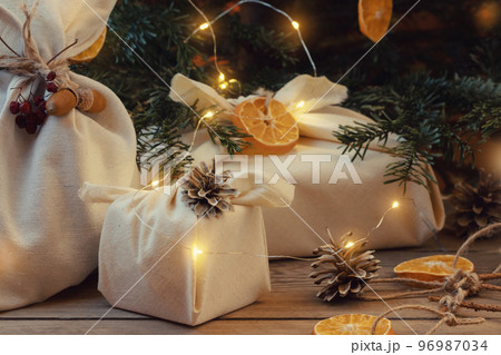 Zero waste christmas concept. Packed in natural fabric gifts and decorations from natural materials with christmas lights on a wooden table 96987034