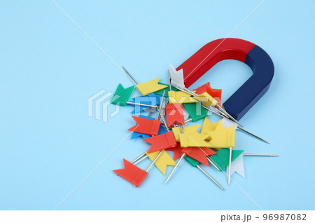 Magnet attracting colorful pins on light blue background 96987082