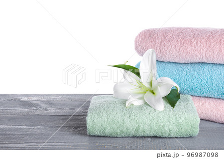 Fresh towels and lily flower on grey wooden table against white background. Space for text 96987098