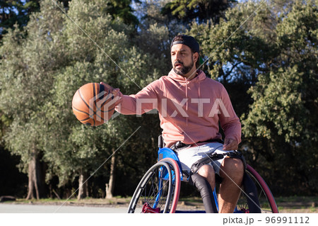 Bearded man in sports wheelchair dribbling basketball Bearded man in sports wheelchair dribbling basketball 96991112