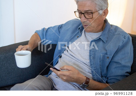 Senior man looking at phone screen while sitting in armchair Senior man looking at phone screen while sitting in armchair 96991128