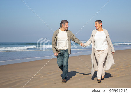 Senior couple walking along seashore 96991212
