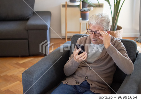 Senior man adjusting glasses while reading sms Senior man adjusting glasses while reading sms 96991664