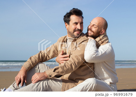 Smiling bald man sitting on sand with boyfriend 96991679