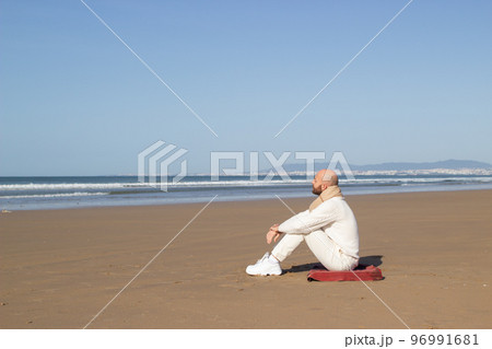 Lonely middle aged man in scarf sitting on beach 96991681