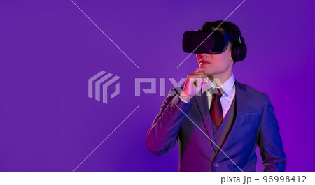 Asian businessman in white shirt red tie and jacket suit wear vr glasses virtual reality headset posing watching thinking on purple color background. Asian businessman in white shirt red tie and jacket suit wear vr glasses virtual reality headset posing watching thinking on purple color background. 96998412